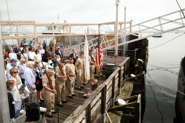 Veterans and guests stand for pledge of allegiance on dock at Mayflower II.