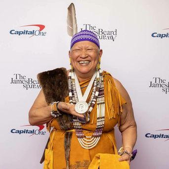 Sherry Pocknett dressed in regalia holds James Beard award.