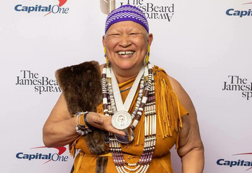 Sherry Pocknett dressed in regalia holds James Beard award.