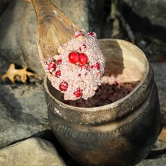 Nasaump with cranberries cooks over an outdoor fire. A Museum educator lifts some of the mixture on a wooden spoon.