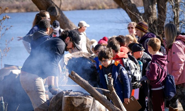 Museum educator demonstrates a mishoon burn on the Historic Patuxet Homesite during the fall to a group of children.