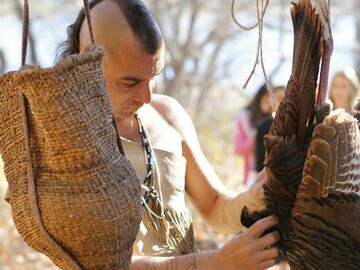 Museum educator dressed in regalia examines a turkey on the Historic Patuxet Homesite.