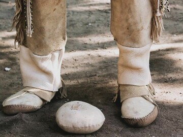 A Wampanoag person in regalia stands near a game ball.