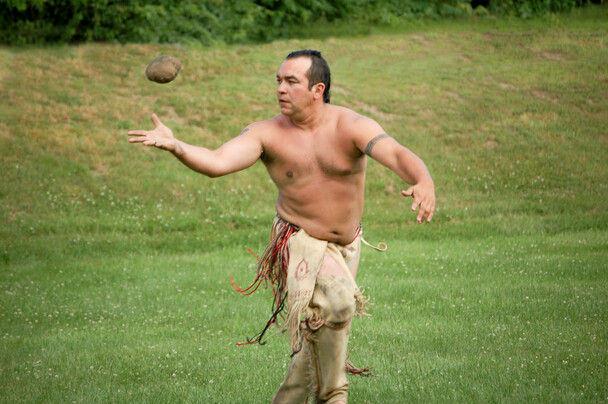 Wampanoag man dressed in regalia plays sports in a grassy field