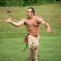 Wampanoag man dressed in regalia plays sports in a grassy field