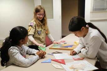 Three students engaged with learning materials around a classroom table.