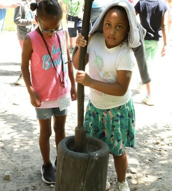 A young girl pounds corn on the Historic Patuxet Homesite.