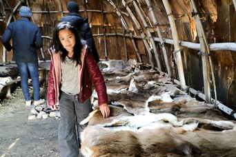 A young girl feels fur on lined benches inside the wetu.