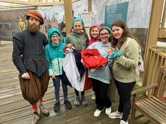 School children stand on wooden pier leading to Mayflower II with a Pilgrim.