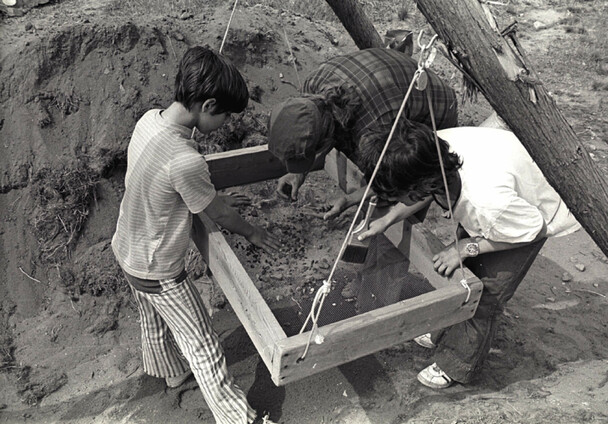 An archaeologist and two children look through fragments in a sieve on the Allerton-Cushman Site.