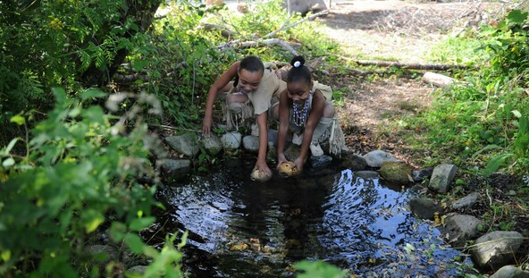 Two girls dressed in Wampanoag regalia gather water from a spring on the Historic Patuxet Homesite.