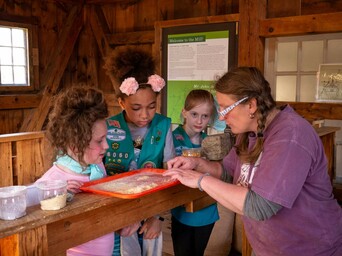 Young girls wearing Scout uniforms learn about different kinds of milled corn at the Plimoth Grist Mill.