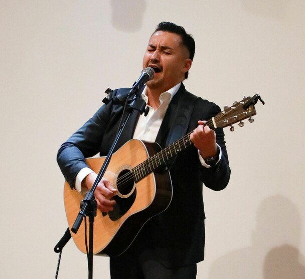Man in a suit play guitar and sings into a microphone.