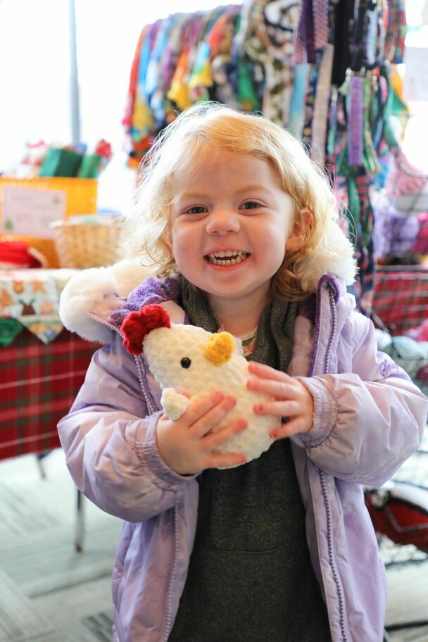 A small child at the winter fair holds a handmade stuffed animal chicken.