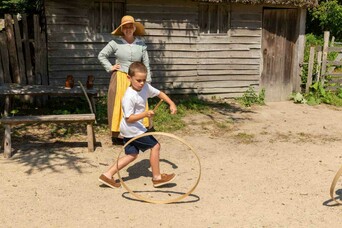 Boy plays with a wooden hoop in front of a Pilgrim