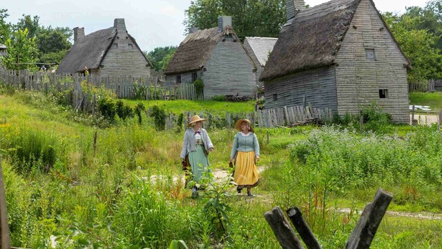 Two pilgrim women walking in back of houses