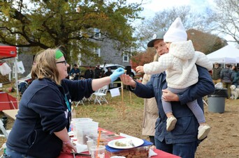 Plimoth Grist Mill Educator gives sample baked good to a father holding his young daughter.