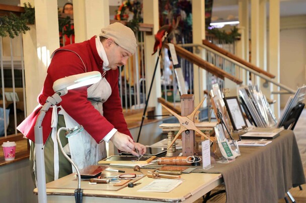 A man dressed in period clothing stands at a table displaying his historic craft.