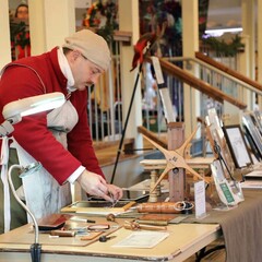 A man dressed in period clothing stands at a table displaying his historic craft.