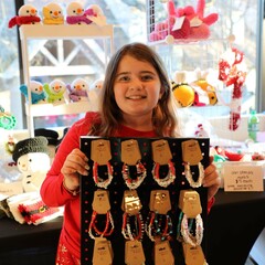 A crafter holds up a display of friendship bracelets that she has made.