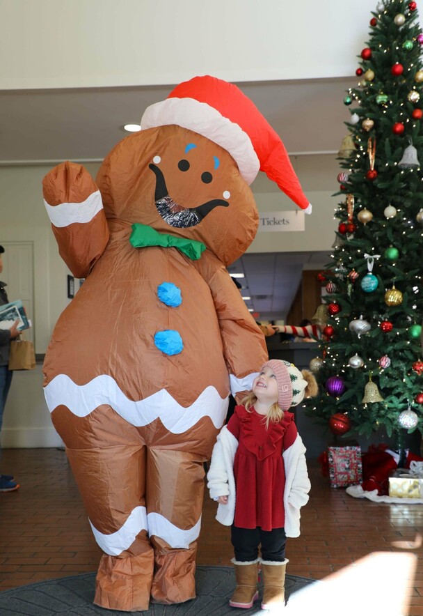 A young stands near a gingerbread man near a decorated Christmas tree.