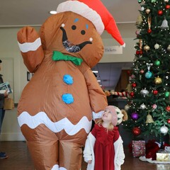 A young stands near a gingerbread man near a decorated Christmas tree.