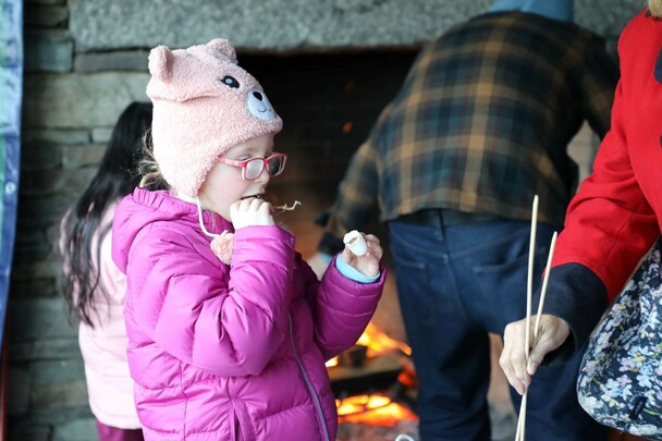 A young girl in a purple jacket and hat enjoys s'mores.