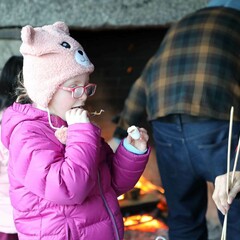 A young girl in a purple jacket and hat enjoys s'mores.