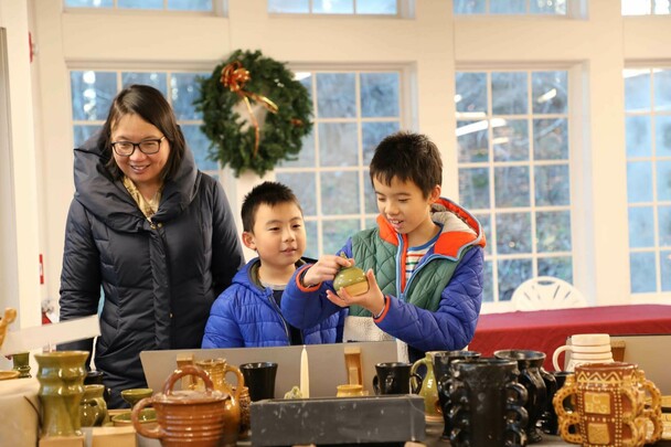 Two young boys examine Plimoth Patuxet Pottery as they stand near their mother.