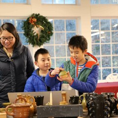 Two young boys examine Plimoth Patuxet Pottery as they stand near their mother.