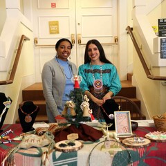 Two Indigenous Artisan Fellows stand behind a table displaying their art.