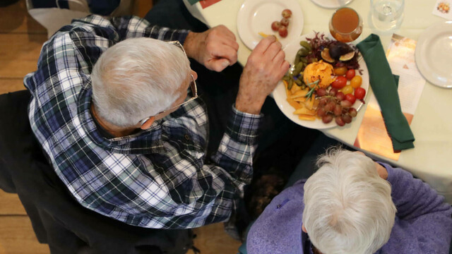 A couple eats a plate of cheese and fruit at set table.