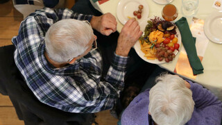 A couple eats a plate of cheese and fruit at set table.