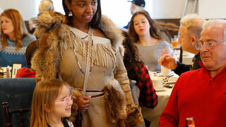 Indigenous Educator in Wampanoag regalia greets Thanksgiving guests