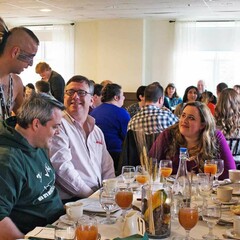 Indigenous Educator dressed in regalia speaks with guests seated for Thanksgiving dinner.
