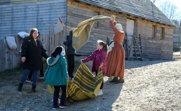 Two young girls and their mother help a Pilgrim woman with laundry in Plymouth Colony.