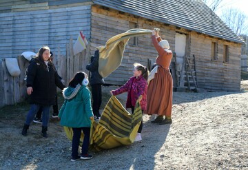 Two young girls and their mother help a Pilgrim woman with laundry in Plymouth Colony.