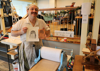 Artisan in historic dress holds up print he has created using historic methods
