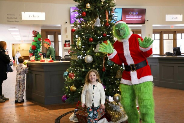 Child poses in front of a decorated Christmas tree with the Grinch