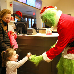 The Grinch gives a young girl a candy cane.