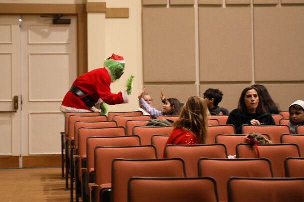 The Grinch high-fives children seated in a movie theater.