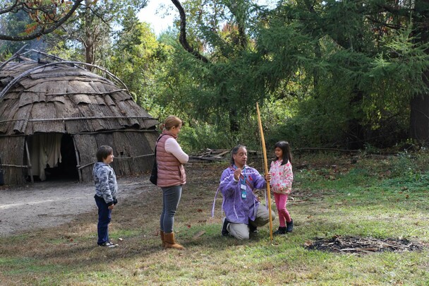 An Educator on the Historic Patuxet Homesite teaches young guests archery beside the winter wetu.