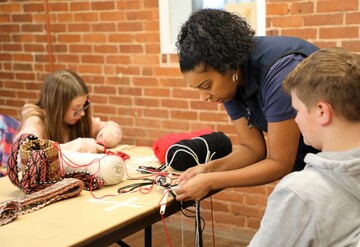 Educator demonstrates finger weaving to young learners.