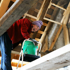 A Museum staffer stands in the eaves of a Pilgrim House with a green bucket as she works to daub walls.