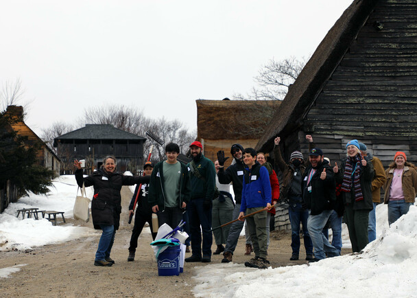 A group of volunteers standing in the English Village smile and wave.