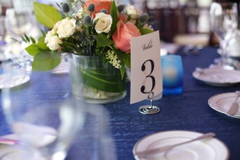 A set table with a floral centerpiece, blue tablecloth, and number three.