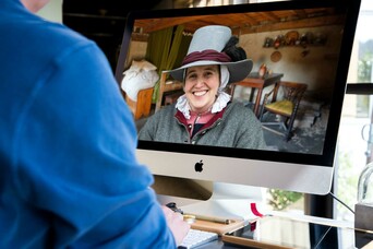 Person in blue shirt uses a computer that has a smiling Pilgrim on the screen