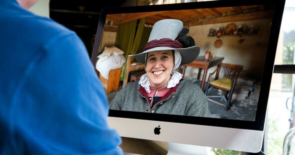 Person in blue shirt uses a computer that has a smiling Pilgrim on the screen