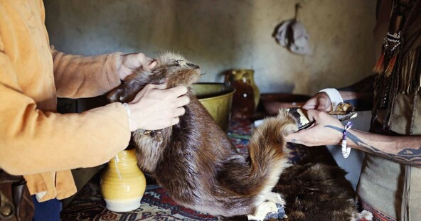 A Wampanoag man and a Pilgrim man trade items inside an English style house.