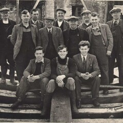 Men pose within partially constructed boat hull